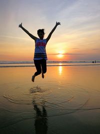 Man jumping on beach against sky during sunset