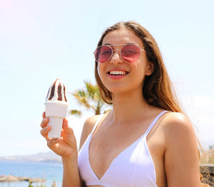 Portrait of smiling woman holding sunglasses against sky