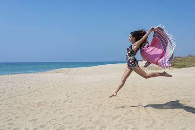 Full length of girl jumping with fabric at beach