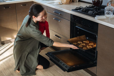 Family, mom with toddler baby girl cooking gingerbread and puts cookies in oven. christmas homemade