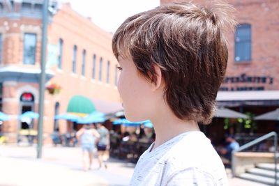 Side view of boy standing on street during sunny day