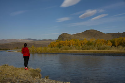 Rear view of man standing by lake against sky