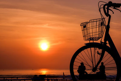 Silhouette bicycle by sea against sky during sunset