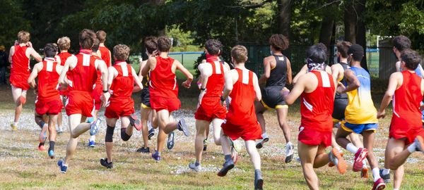Group of people running on grassland against trees