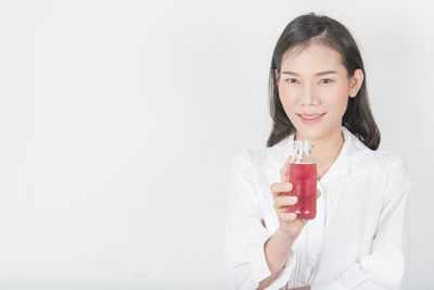 Portrait of a smiling young woman drinking glass against white background