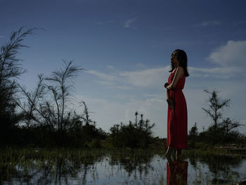 Side view of woman standing by lake against sky