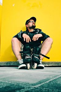 Bearded man with glasses and his roller blades sitting by the yellow statue