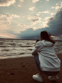 Rear view of woman photographing sea against sky at sunset