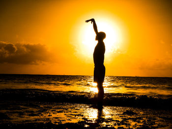 Silhouette man with hand raised standing at beach against sky during sunset