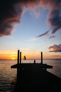 Silhouette people on pier over sea against sky during sunset