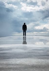 Rear view of silhouette man standing by sea against sky