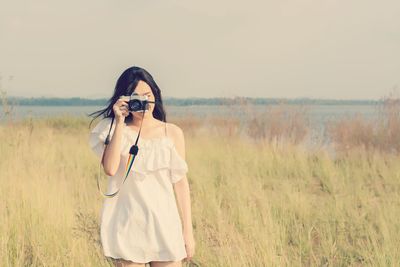 Young woman photographing on grassy field