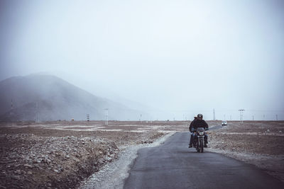 Rear view of man riding motorcycle on road against sky