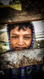 Close-up portrait of girl seen through wooden fence