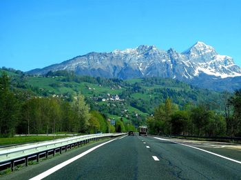 Road amidst trees and mountains against clear sky