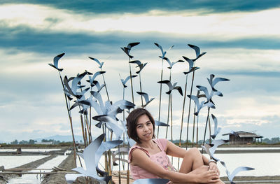 Portrait of young woman sitting by sea against sky