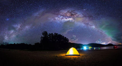 Illuminated tent on beach against sky at night