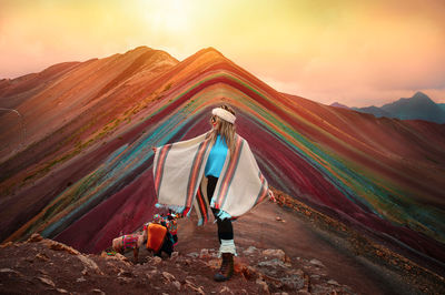 Full length of multi colored umbrellas on desert against sky during sunset