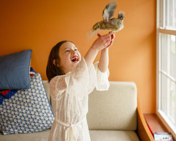 A child laughs with delight holding a flapping bird aloft in her hands