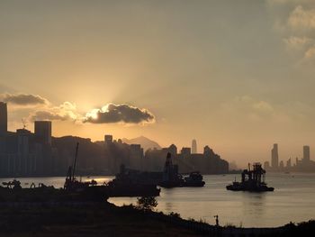 Silhouette buildings by sea against sky during sunset