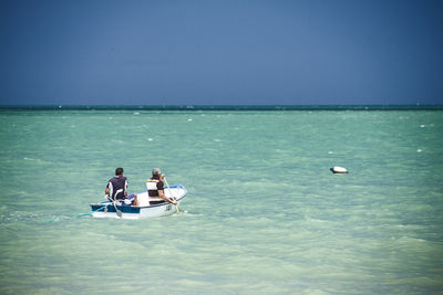 Two people in boat on sea against clear sky