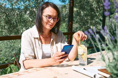 Woman checking social media in smartphone during summer morning breakfast in cafe bar outdoors.