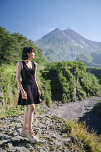 Full length of woman looking away while standing on rock against mountains and sky