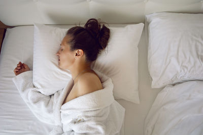 Woman in a white robe is lying on the bed and sleeping near window in hotel apartment after a shower