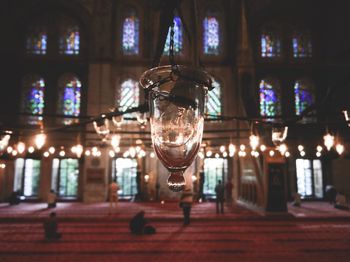 Close-up of illuminated lamp hanging on glass window in mosque