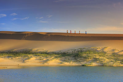 People on sand dune against sky