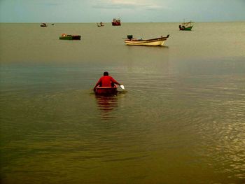 Rear view of fisherman sitting in boat on sea during sunset