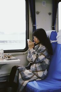 Side view of woman applying lipstick while sitting in train