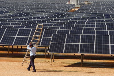 Full length of security guard holding a ladder in front of solar pv panels.