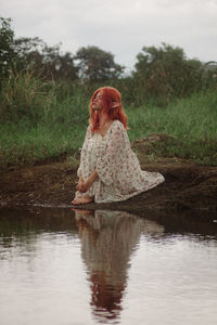 Side view of woman sitting on rock by lake