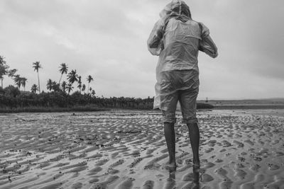 Rear view of person wearing raincoat standing on beach