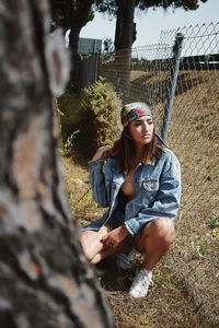 Young woman looking away while crouching by fence