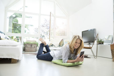 Mature woman lying on floor, using smartphone