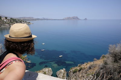 Woman wearing straw hat on cliff by sea at capo zafferano