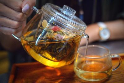Cropped hand of woman pouring herbal tea in cup