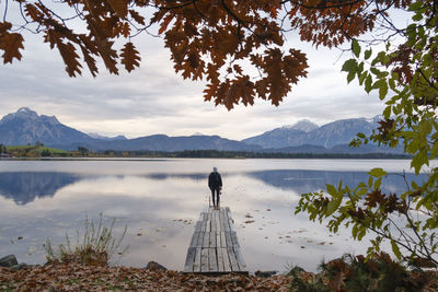 Rear view of woman standing on pier by lake against sky