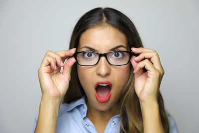 Close-up portrait of shocked young woman wearing eyeglasses against gray background