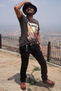 Young man wearing sunglasses standing on railing against sky