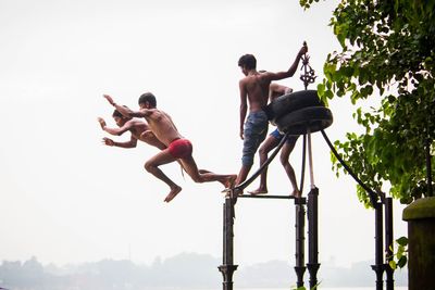 Low angle view of men jumping against sky
