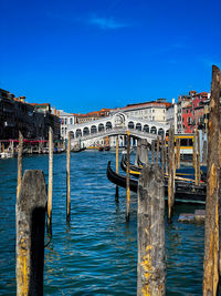 Wooden post in canal amidst buildings against blue sky