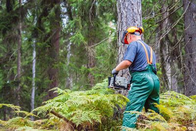 Full length of man standing by tree trunk in forest