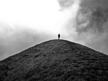 Low angle view of man standing on mountain against cloudy sky