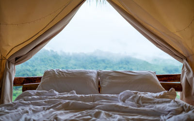 A white cosy bed in a tent with a beautiful nature view on foggy day outside