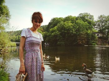 Woman standing by lake against trees