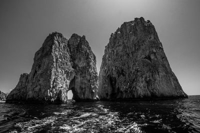 Rock formation in sea against clear sky