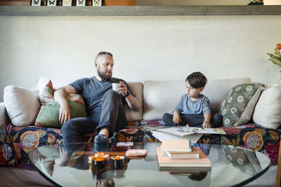 Father holding coffee mug while assisting son in doing homework at home